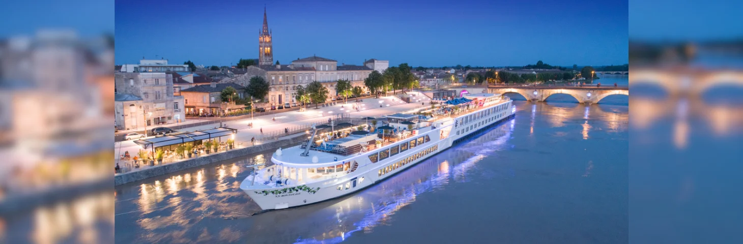 A Uniworld river cruise vessel docked in Libourne, France at dusk.