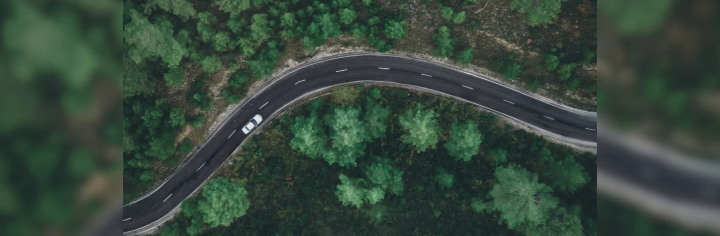 A white car driving along a curved two-way road lined with trees.