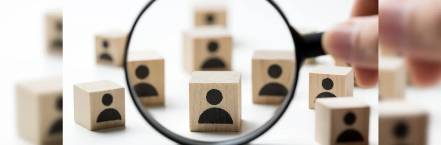 A magnifying glass looking at wooden cubes with silhouettes of people on.